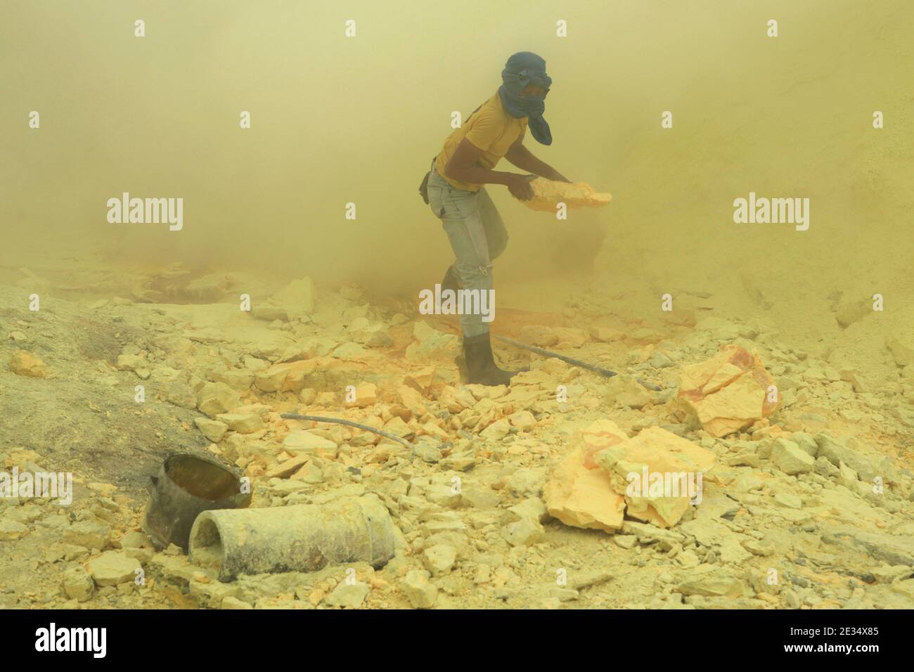 Miner sammelt Schwefel in den Wolken vulkanischen Gases in den Schwefelminen im Krater des aktiven Vulkans Kawah Ijen in Ost-Java, Indonesien. Jeden Morgen klettern zwei hundert Bergarbeiter auf den Grund des Kraters für die nächste Ladung Schwefel. Sie füllen ihre Körbe manuell mit Schwefel und tragen diese schwere Ladung dann auf die Füße. Extrem harte Arbeit in den Wolken des giftigen Schwefeldioxids verursacht harten Husten und laufende Augen fast sofort. Die Bergleute arbeiten jedoch ohne jeglichen Schutz. Nur wenige von ihnen haben Gasmasken. Jeder Bergmann verdient rund 10 US-Dollar pro Tag. Stockfoto