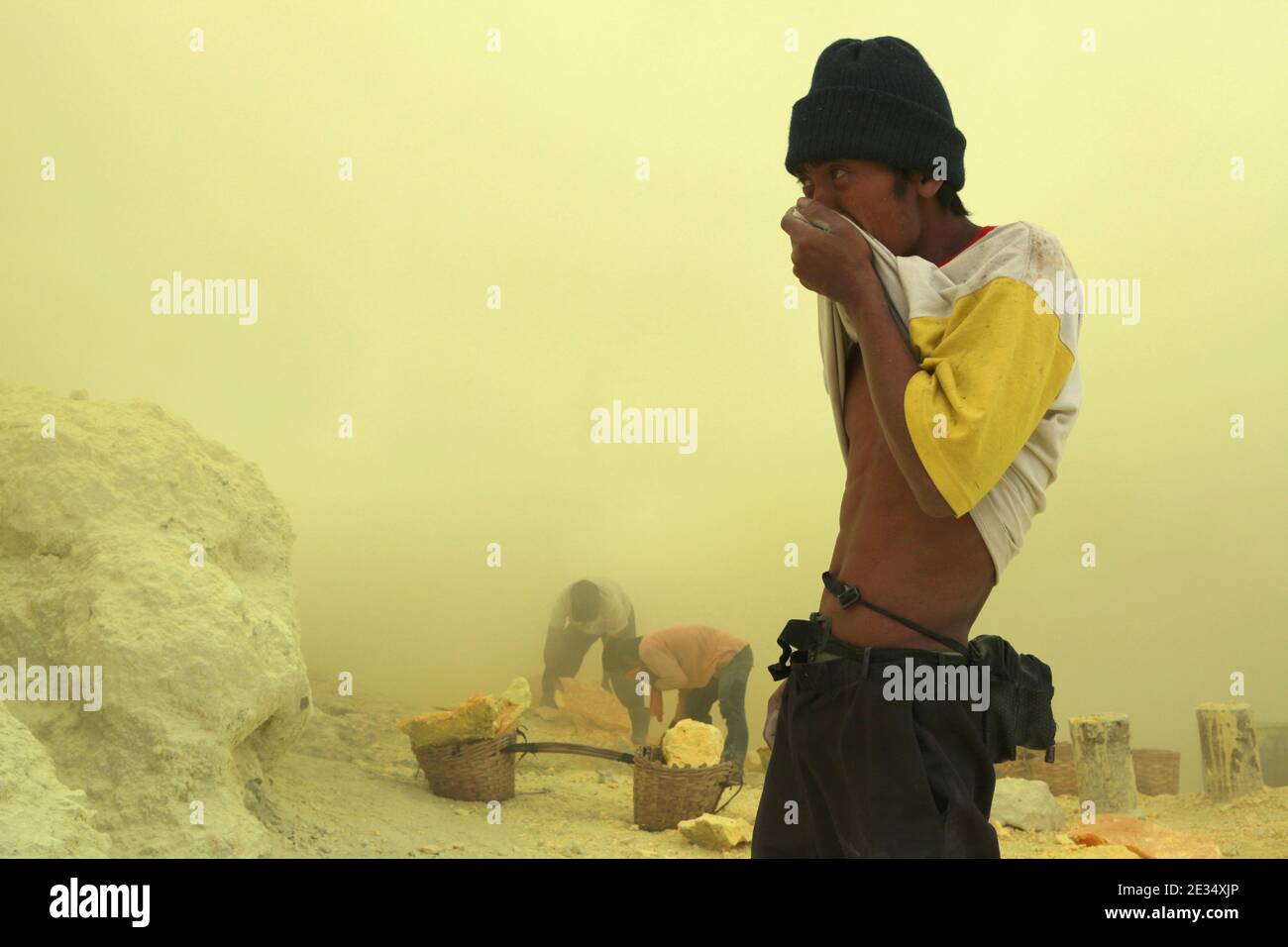 Miner versucht, sich vor den Wolken vulkanischen Gases in den Schwefelminen im Krater des aktiven Vulkans Kawah Ijen in Ost-Java, Indonesien, zu retten. Jeden Morgen klettern zwei hundert Bergarbeiter auf den Grund des Kraters für die nächste Ladung Schwefel. Sie füllen ihre Körbe manuell mit Schwefel und tragen diese schwere Ladung dann auf die Füße. Extrem harte Arbeit in den Wolken des giftigen Schwefeldioxids verursacht harten Husten und laufende Augen fast sofort. Die Bergleute arbeiten jedoch ohne jeglichen Schutz. Nur wenige von ihnen haben Gasmasken. Jeder Bergmann verdient etwa 10 US-Dollar pro Tag Stockfoto