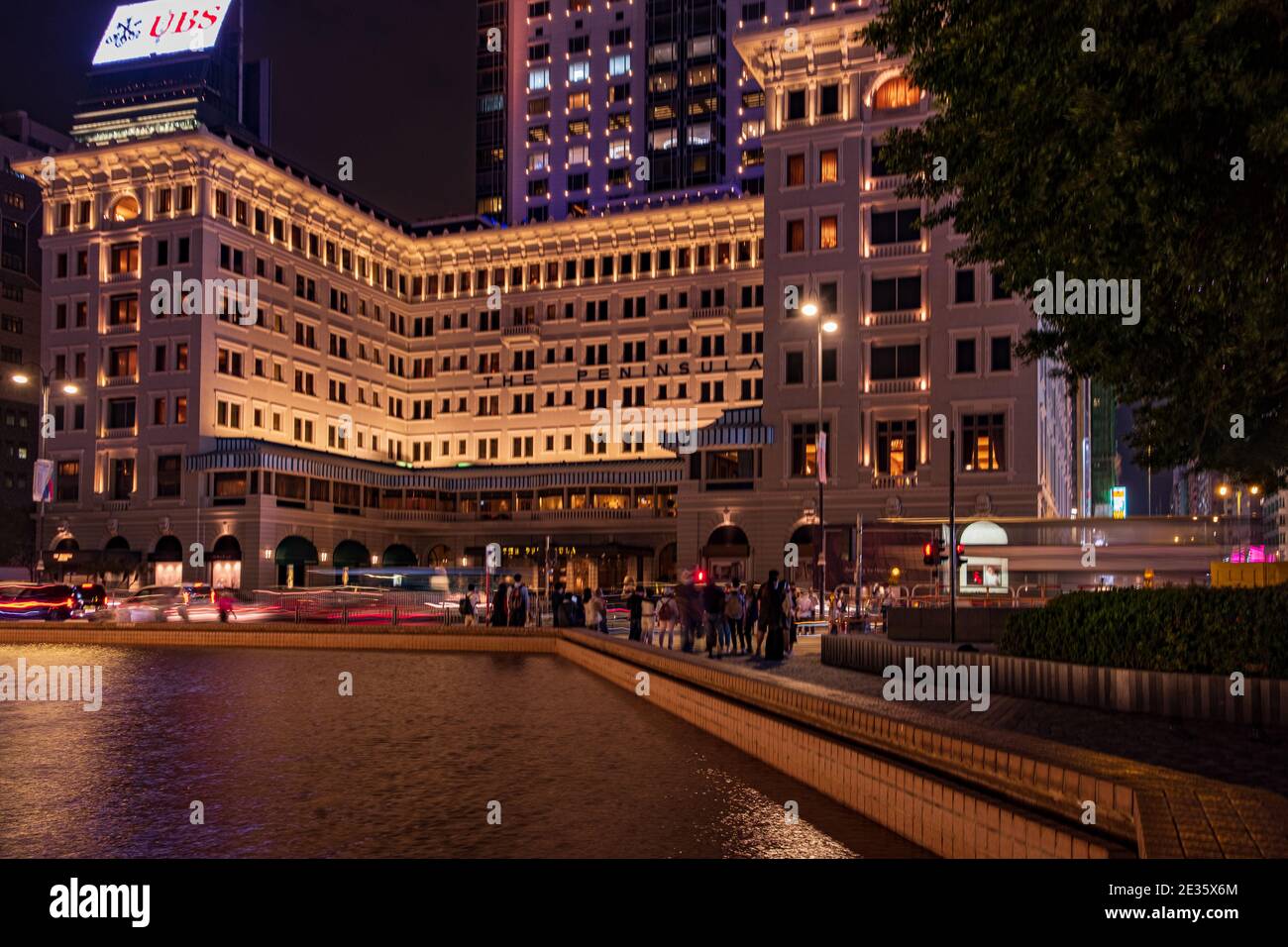 Wenn der Abend über dem Peninsula Hotel fällt, reflektiert das sanfte Leuchten der Lichter der Stadt vom Brunnen. Stockfoto