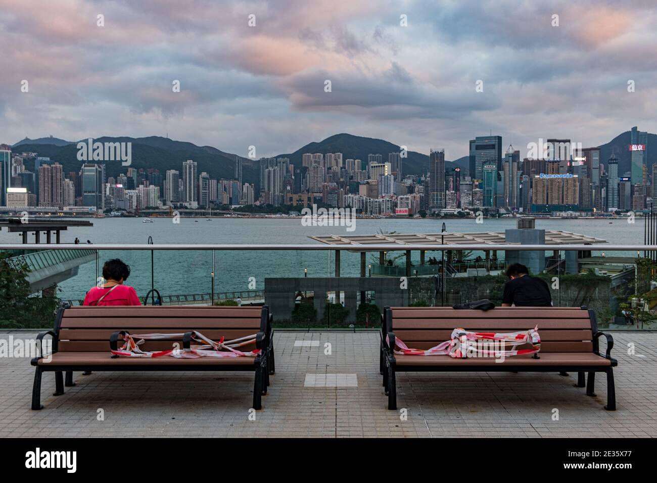 Urbane Uferszene mit Fußgängern, die während der Pandemie entlang einer Promenade spazieren, und der Skyline von Hongkong im Hintergrund. Stockfoto Urbane Uferszene mit Fußgängern, die während der Pandemie entlang einer Promenade spazieren, und der Skyline von Hongkong im Hintergrund. Stockfoto
