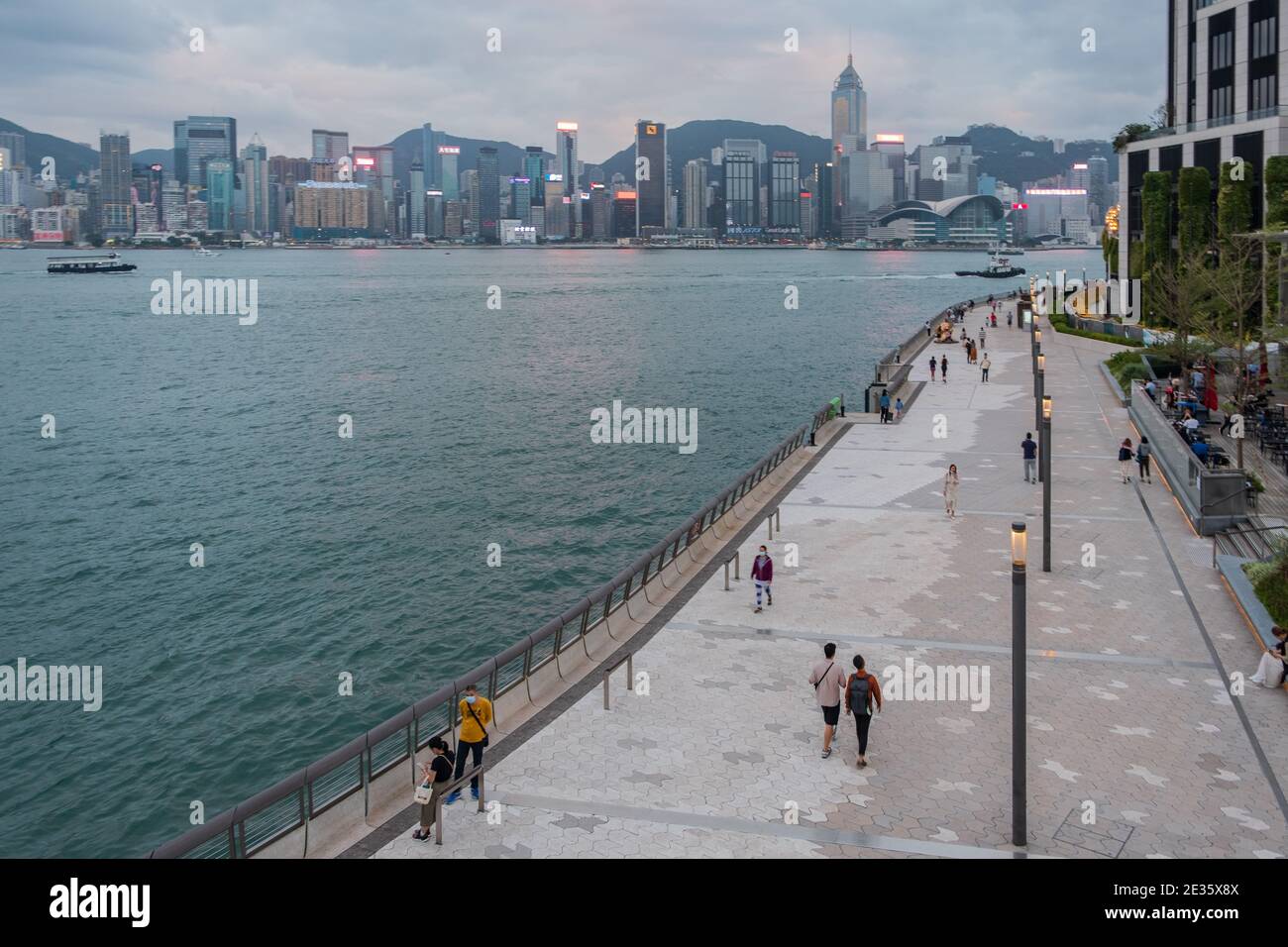 Urbane Uferszene mit Fußgängern, die entlang einer Promenade spazieren gehen, und die Skyline von Hongkong im Hintergrund. Stockfoto Urbane Uferszene mit Fußgängern, die entlang einer Promenade spazieren gehen, und die Skyline von Hongkong im Hintergrund. Stockfoto