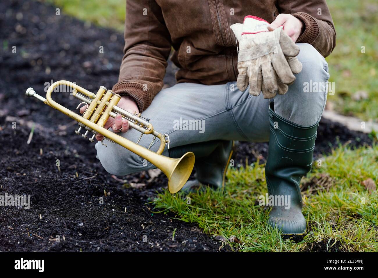 Mannheim, Deutschland. Januar 2021. Johannes Stange, ein Jazztrompeter und angehende Bio-Bauer, sitzt mit Trompete und Arbeitshandschuhen an einem Knoblauchpflanzenbett. Angesichts der Absage von Konzerten aufgrund der Corona änderte er seine Karriere und schuf eine zweite wirtschaftliche Stütze mit Gartenarbeit. Quelle: Uwe Anspach/dpa/Alamy Live News Stockfoto