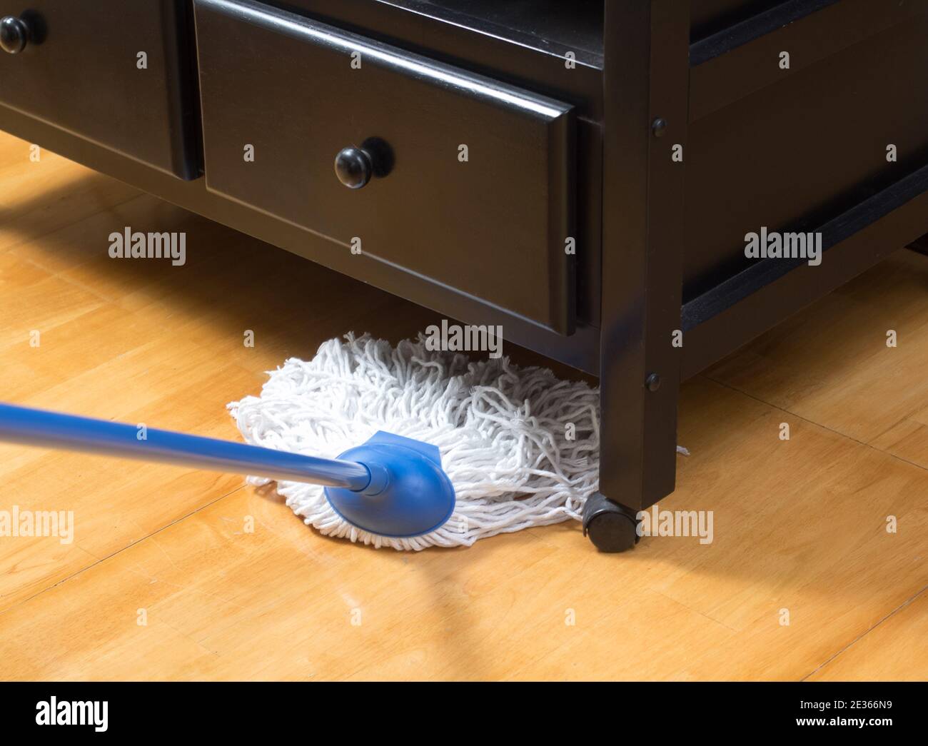Haushälterin wischen Holzboden mit Mopp unter dem Schrank Stockfoto