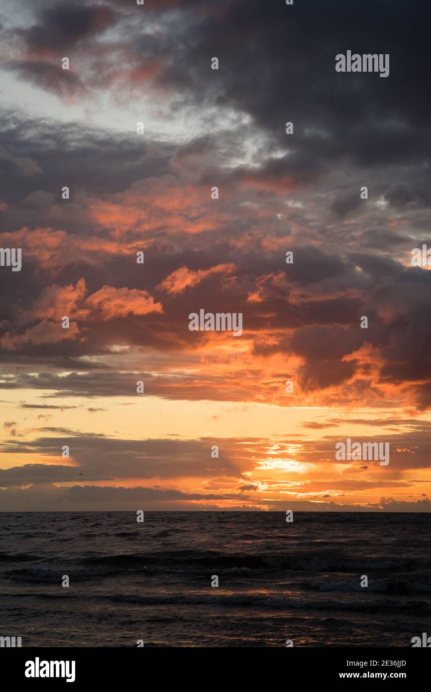 Schönes warmes Sonnenuntergangslicht in den Wolken über der ostsee Vertikal Stockfoto