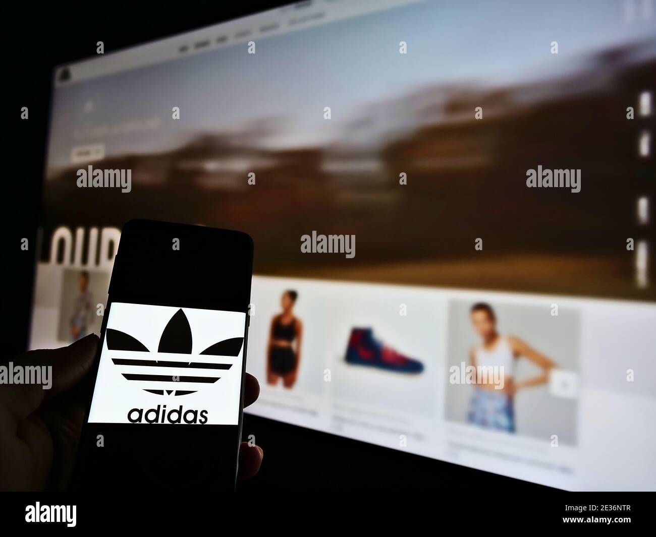 Person, die Smartphone mit Logo der deutschen Sportbekleidung (Schuhe, Kleidung, Accessoires) Hersteller Adidas hält. Konzentrieren Sie sich auf den Bildschirm des Mobiltelefons. Stockfoto