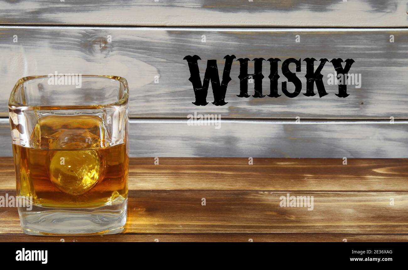 Nahaufnahme eines isolierten Whiskyglases mit Eiswürfel und Holzdielen Hintergrund, Worttext im westlichen Stil (Fokus auf Glas) Stockfoto
