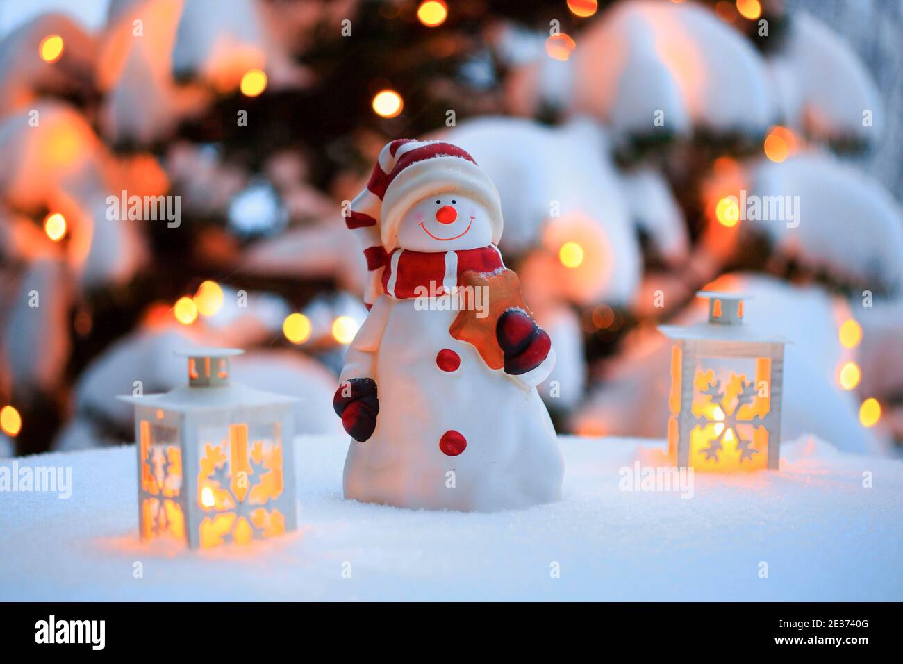 Stimmungsvolle Weihnachtsdekoration im Freien mit Schneemann, Laternen, Schnee und Lichterketten am Weihnachtsbaum Stockfoto