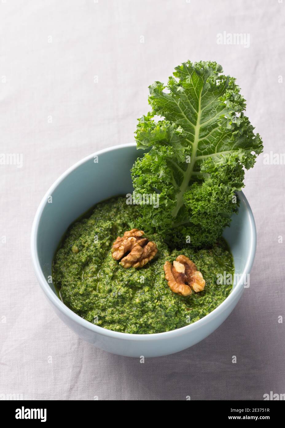 Grünes Pesto aus Grünkohl, Walnüssen, Knoblauch und Olivenöl auf grauem Hintergrund. Leckere gesunde Lebensmittel Stockfoto