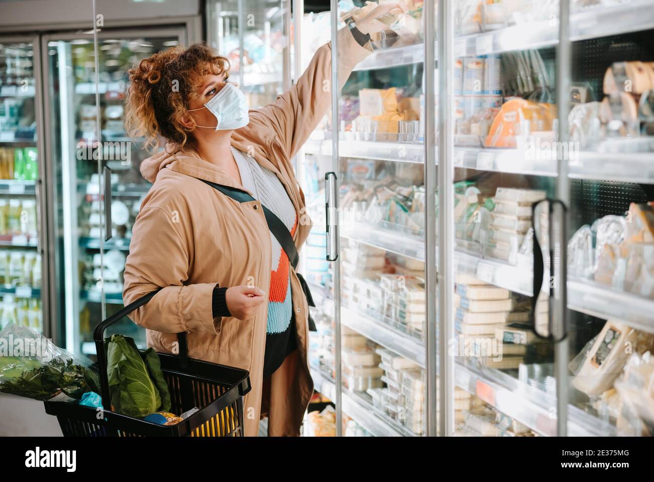 Frau mit Gesichtsmaske kauft Lebensmittel aus einem Supermarkt. Weibliche Kunden einkaufen im Supermarkt während Pandemie. Stockfoto