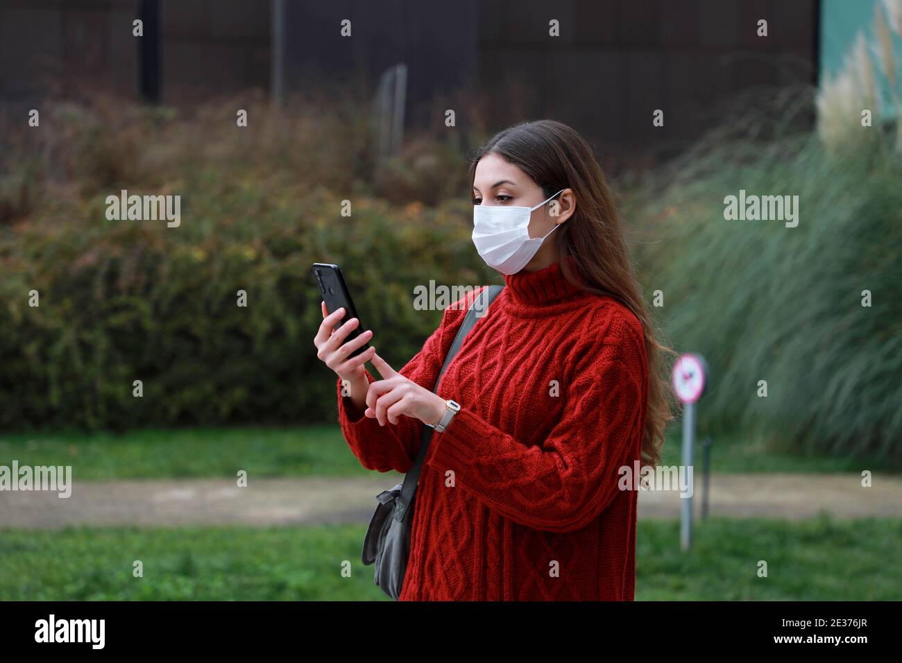 Neuer Normalwert. Besorgte Frau, die Smartphone-App auf Kontaktverfolgung überprüft, wenn sie im Park geht. Stockfoto