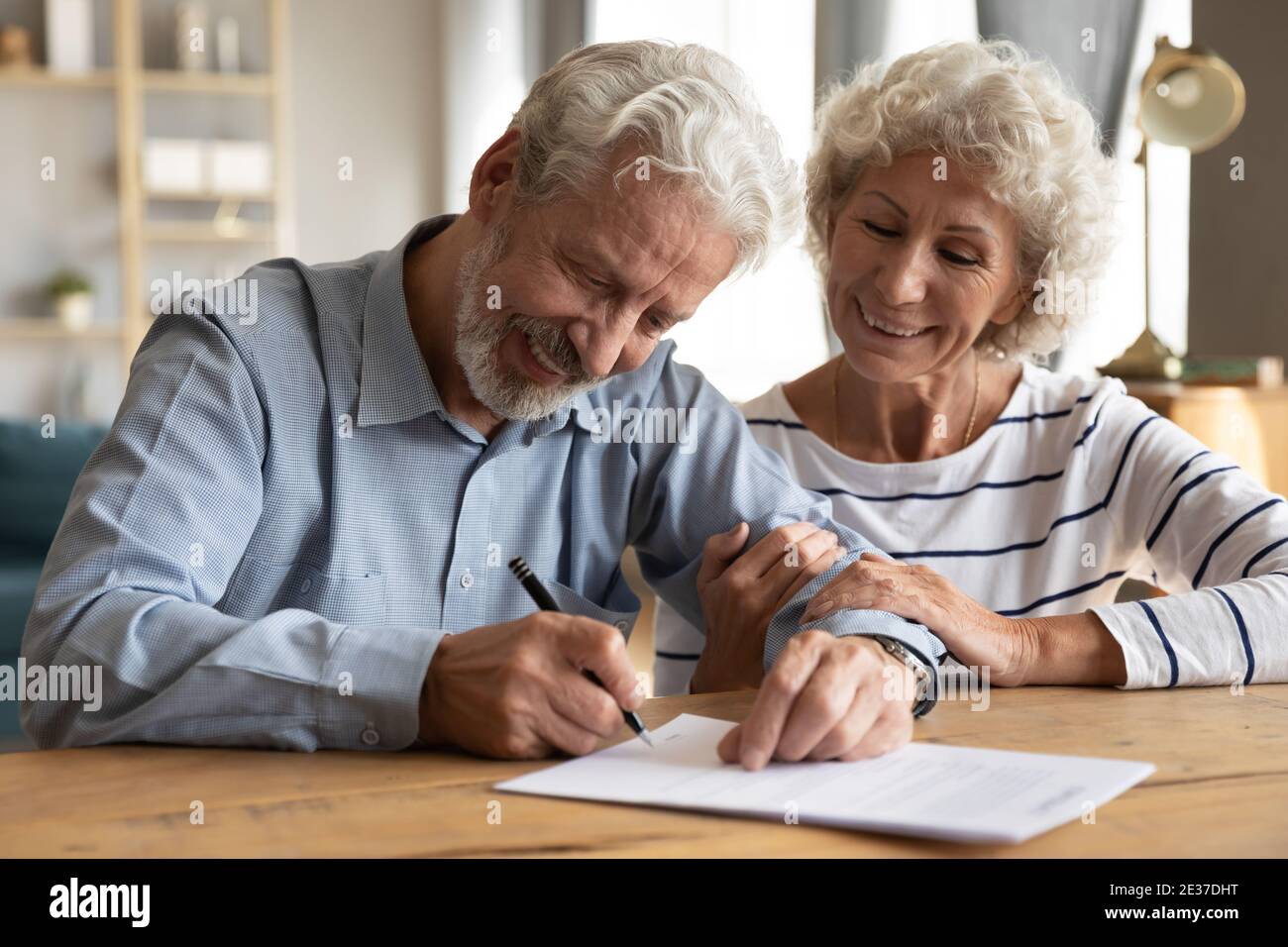 Glückliches altes reifes Rentnerfamilienpaar, das Unterschrift auf Papierdokument setzt. Stockfoto