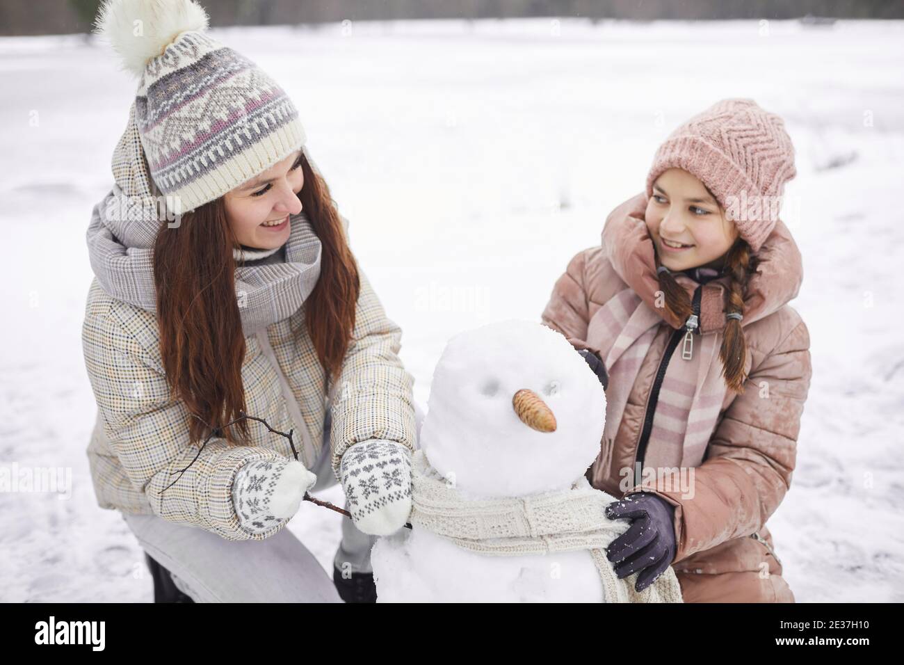 Hochwinkel-Porträt der glücklichen Mutter und Tochter Gebäude Schneemann Zusammen, während Sie Winterurlaub im Freien genießen Stockfoto