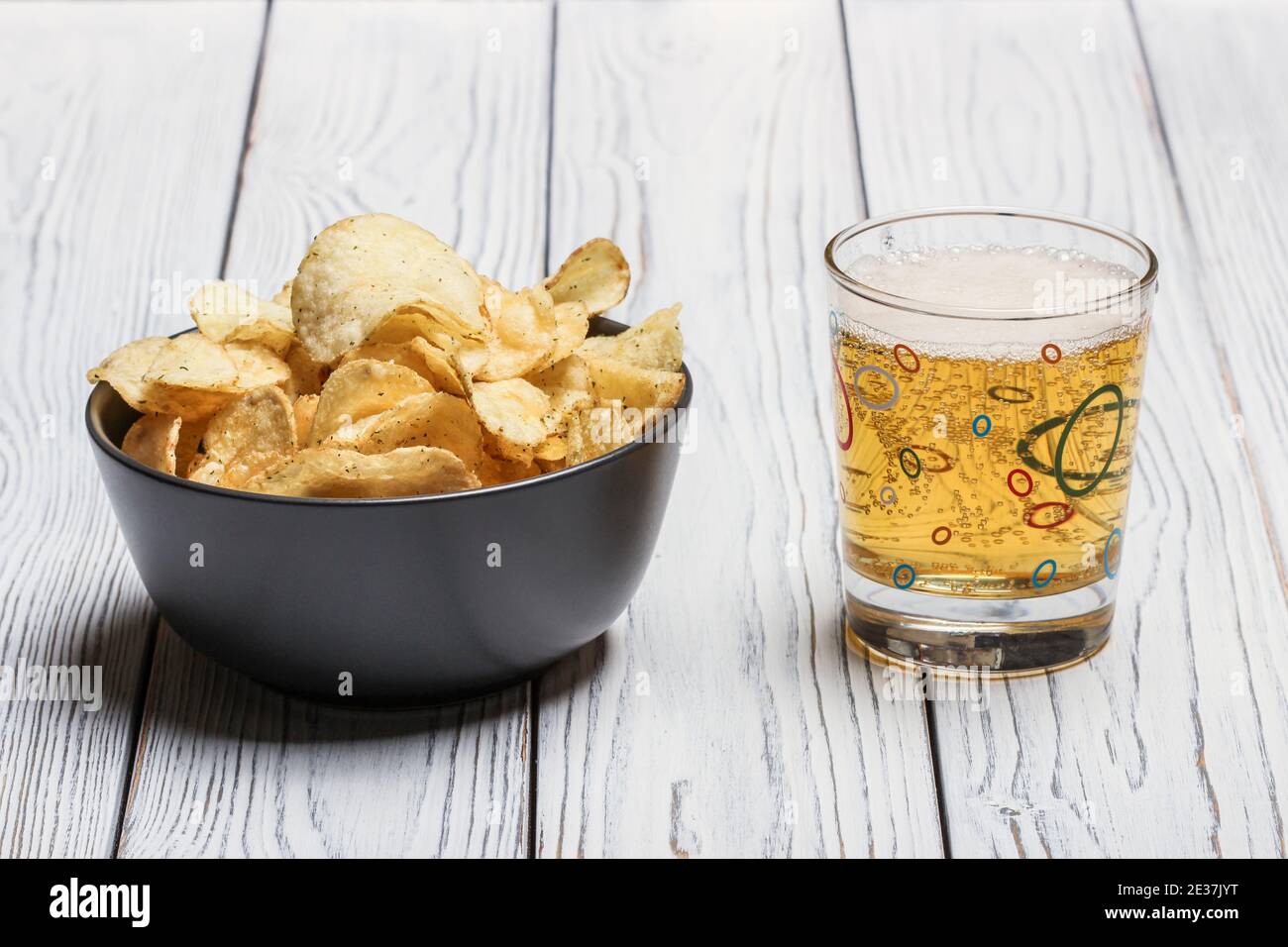 Kartoffelchips in einer Schüssel und Bier in einem Glas Auf einem Holztisch Stockfoto