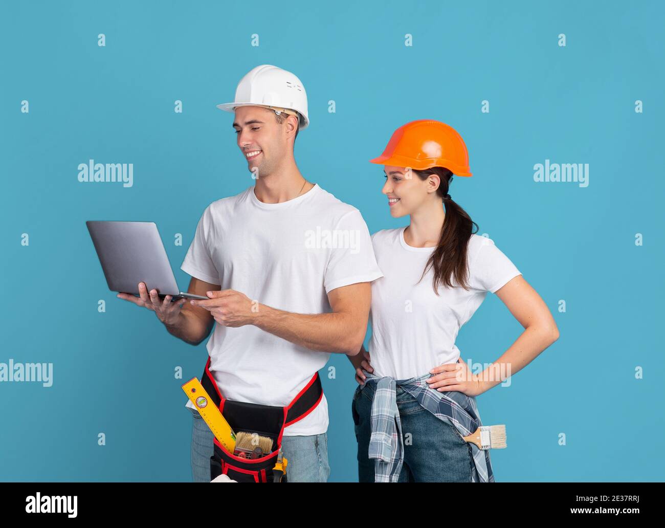 Glückliches junges Paar in Hardhats mit Laptop, Bestellung von Materialien für Reparatur Wohnung Stockfoto