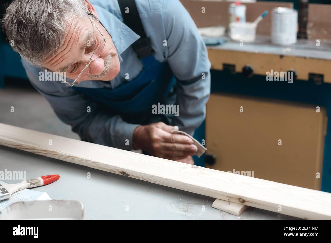 Zimmermannsarbeit in der Schreinerei. Ein älterer männlicher Tischler untersucht sorgfältig ein Holzbrett. Stockfoto
