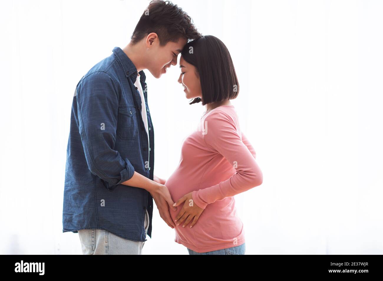 Liebevolle asiatische Mann berühren schwangere Frau Bauch zu Hause stehend Stockfoto