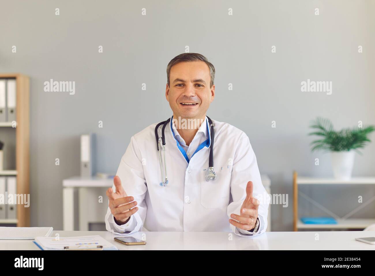 Der männliche Hausarzt sitzt vor der Kamera und gibt seinem Patienten eine Online-Konsultation. Stockfoto