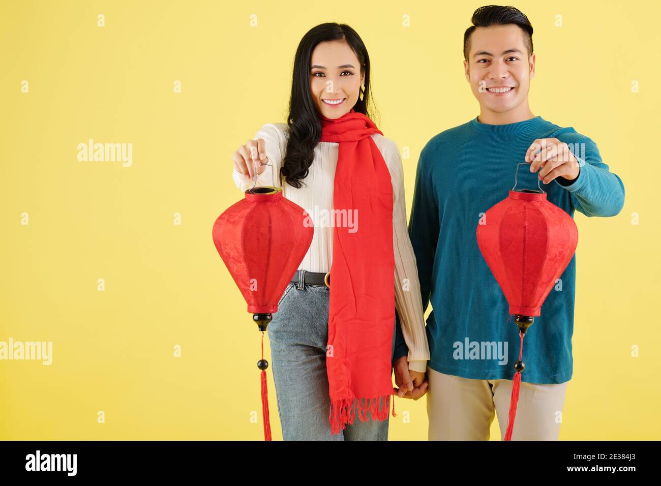Fröhliche vietnamesische Freund und Freundin im Winter Pullover Hände halten Und zeigt rote Papier Lanters für Tet Feier Stockfoto