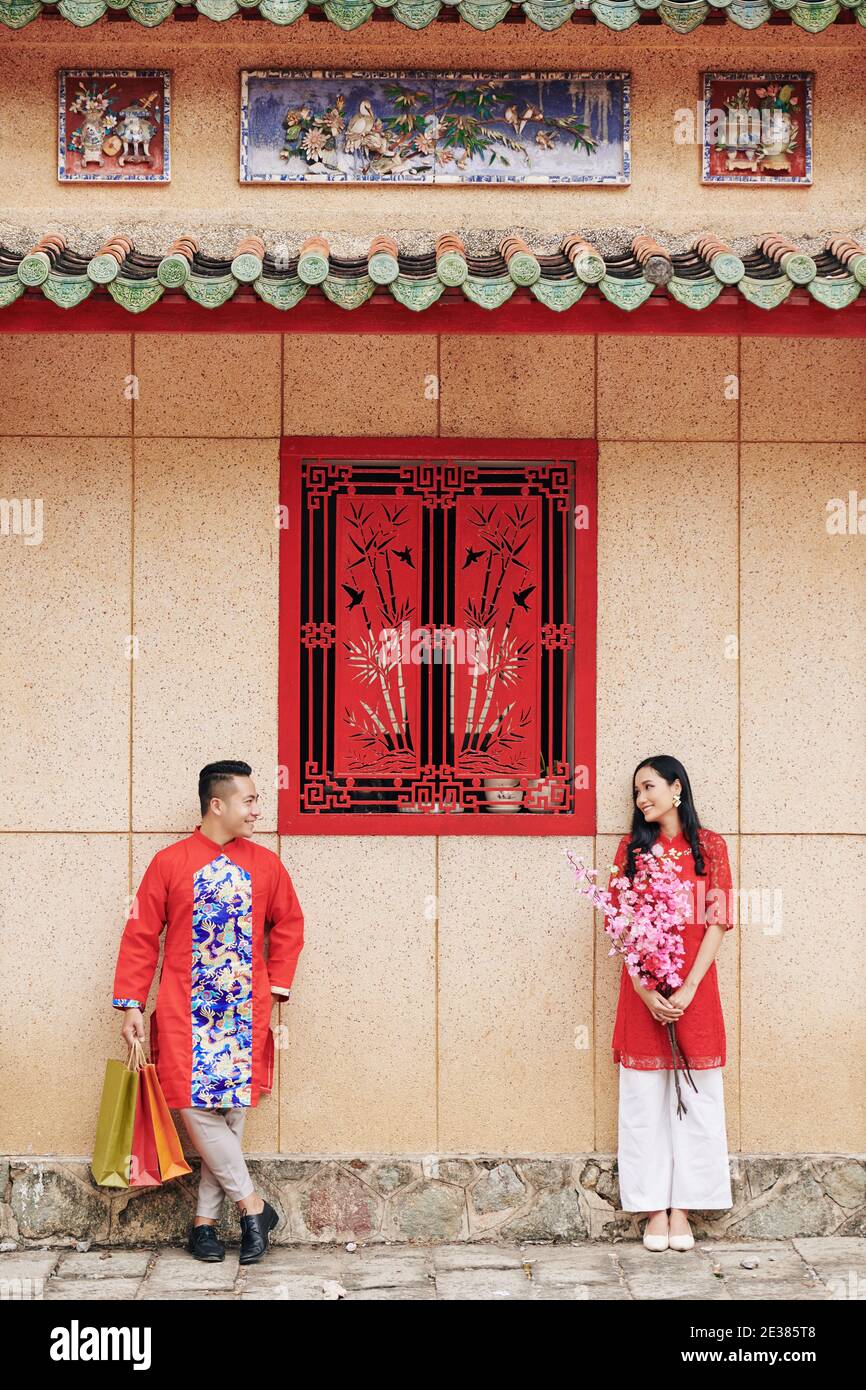 Freund und Freundin in traditionellen vietnamesischen Kleidern stehen im Freien mit Blumen und Einkaufstaschen und einander anschauen Stockfoto