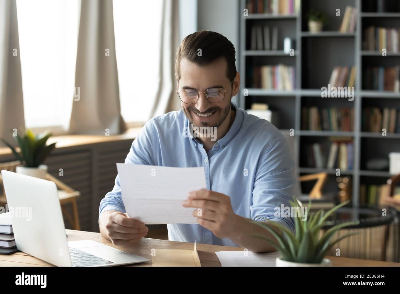 Lächelnder junger Geschäftsmann beim Lesen von Briefpapier im Heimbüro. Stockfoto