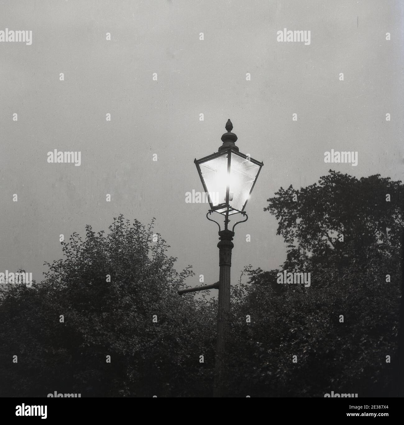 1960s, historisch, Eveningtime und ein Bild einer original viktorianischen Laterne oder Lampe aus Eisen, mit Licht an, England, Großbritannien. Stockfoto