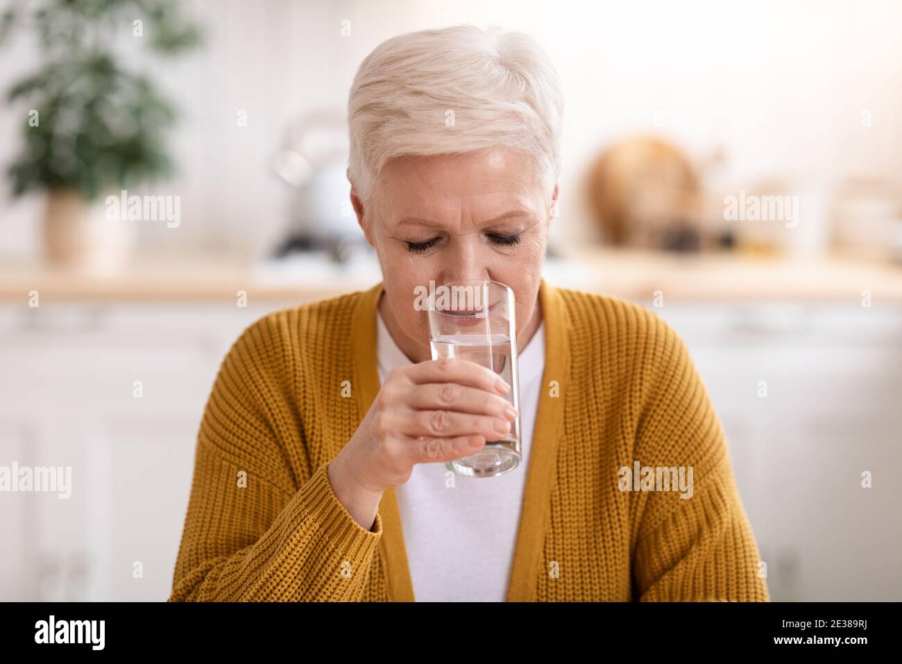 Gut aussehende ältere Dame, die zu Hause stilles Wasser trinkt Stockfoto
