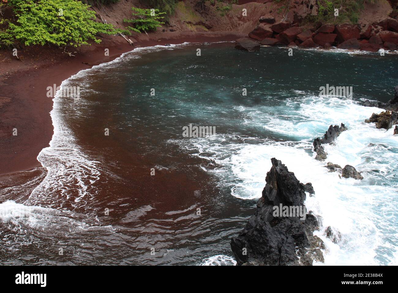 Das türkisfarbene Wasser des Pazifischen Ozeans trifft auf den roten Sand der Kaihalulu Bay in Hana, Maui, Hawaii, USA Stockfoto