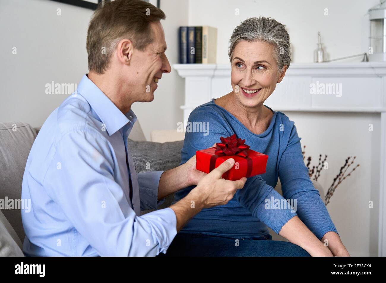 Glücklicher alter Mann gibt rote Geschenkbox an Frau macht Geschenk am Valentinstag. Stockfoto