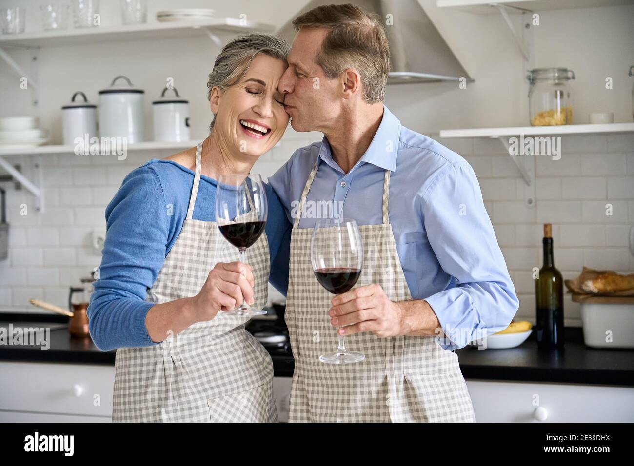 Glückliches älteres Paar umarmt, Wein trinken in der Küche feiern Valentinstag. Stockfoto