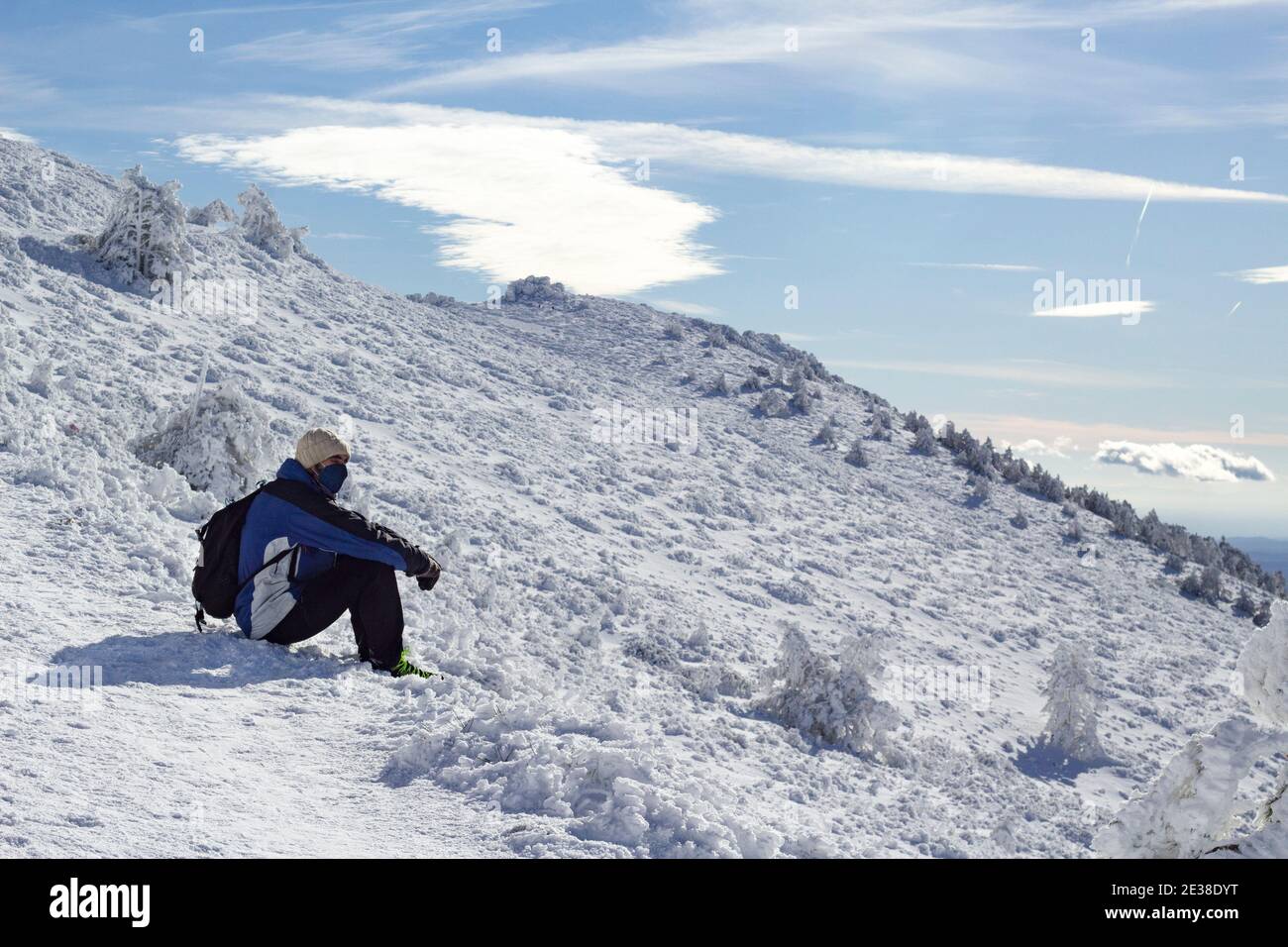 Ein Mann mit Wanderrucksack sitzt im Schneeberg und betrachtet an einem sonnigen Wintertag einen Panoramablick auf die verschneite Landschaft. Er ist müde Stockfoto