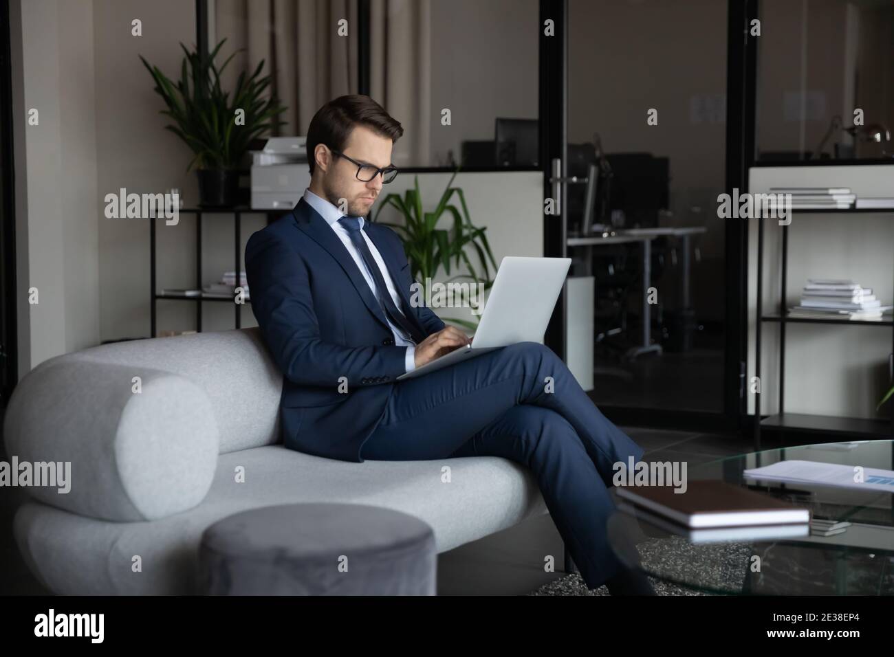 Selbstbewusster Geschäftsmann im Anzug, der im modernen Büro auf einem Laptop arbeitet Stockfoto