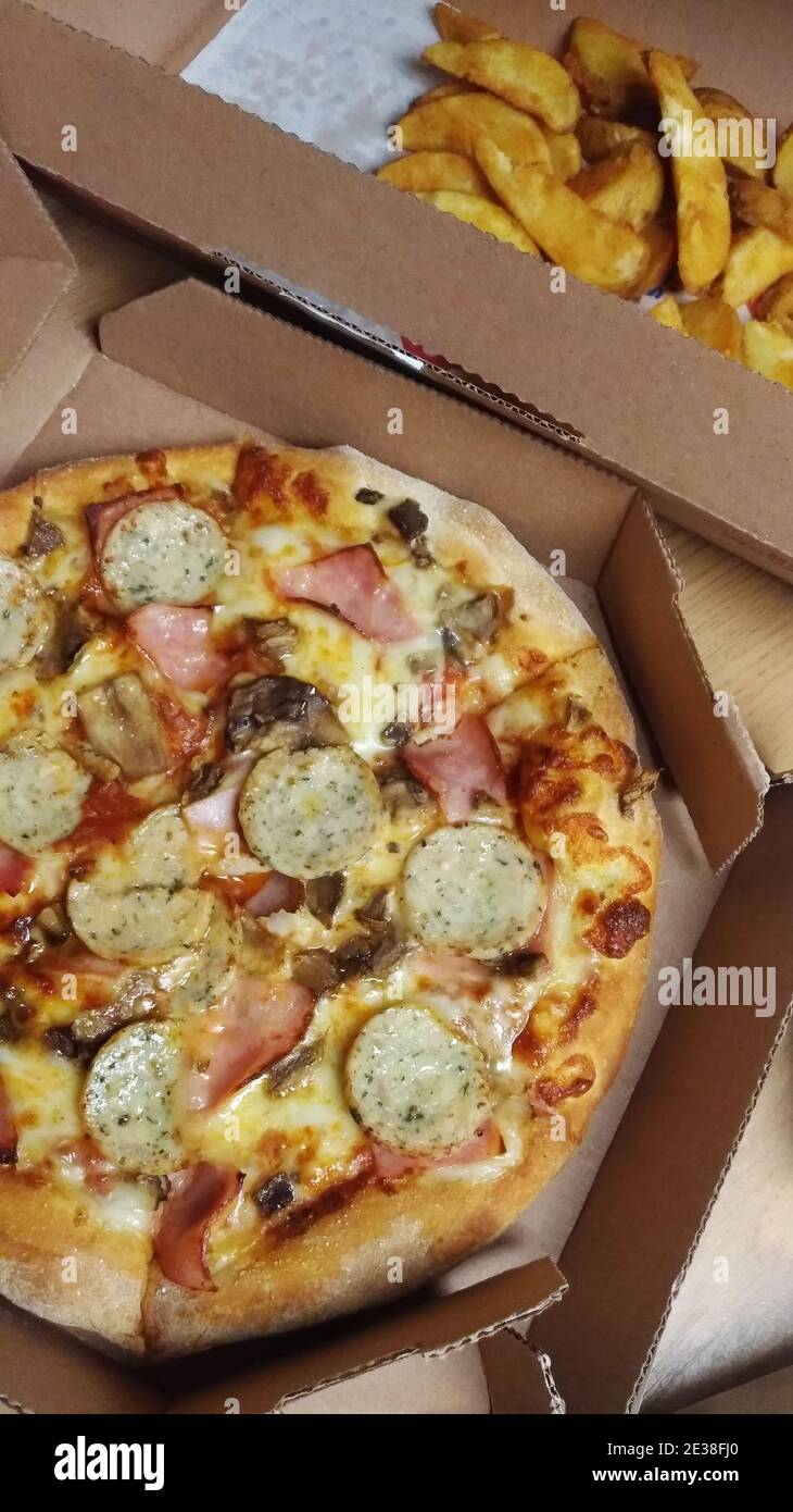 Pizza mit Schinken, Weißwürsten und Bratkartoffeln in Pappkartons Stockfoto