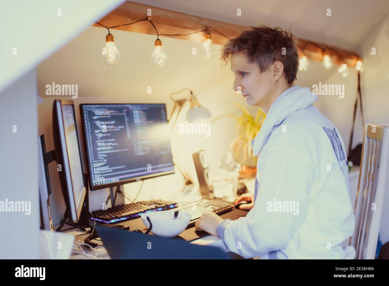 Ein Mann, der an einem Schreibtisch sitzt und von zu Hause aus an seinem Computer arbeitet. IT-Spezialist Programmierer schreiben Code auf seinem pc und Laptop. Entwickler Remote Home Office Stockfoto