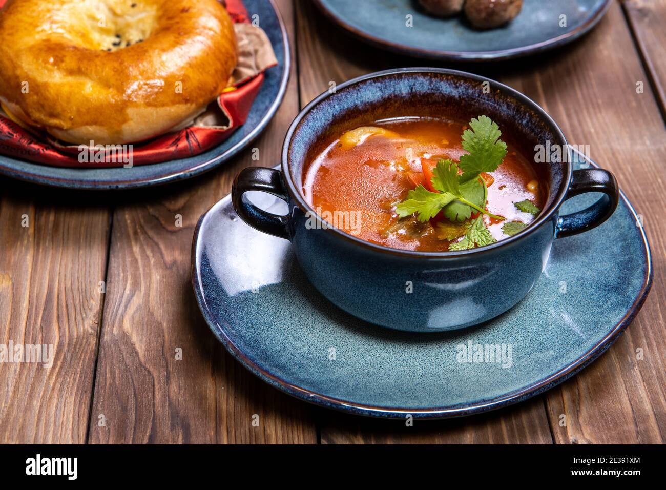 Eine Tasse Suppe, gewürzt mit Kräutern, frischem Gebäck und Bratkartoffeln mit Koteletts auf braunem Holzhintergrund. Stockfoto