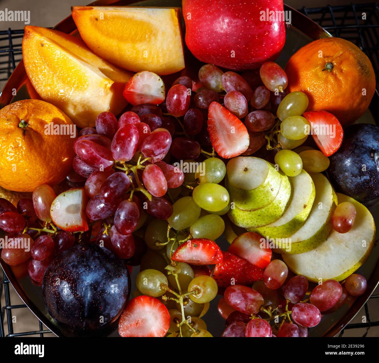 Auf einer Platte stehen verschiedene geschnittene Früchte, rosa und weiße Trauben, Kiwi, Pflaumen, Kaki, Birne, Apfel, Orange, Erdbeere. Der Blick von oben. Stockfoto