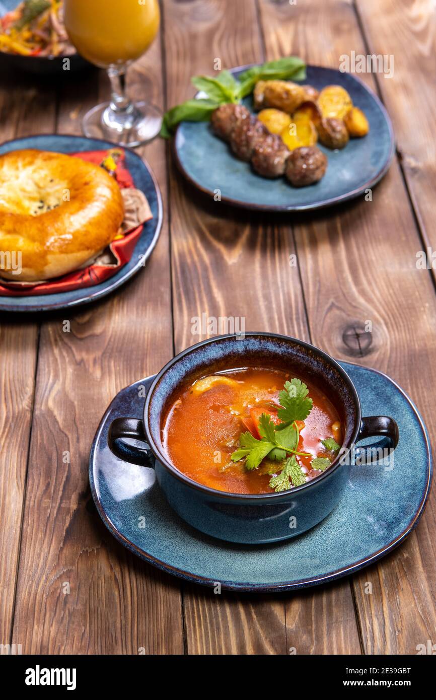 Eine Tasse Suppe, gewürzt mit Kräutern, frischem Gebäck und Bratkartoffeln mit Koteletts auf braunem Holzhintergrund. Stockfoto