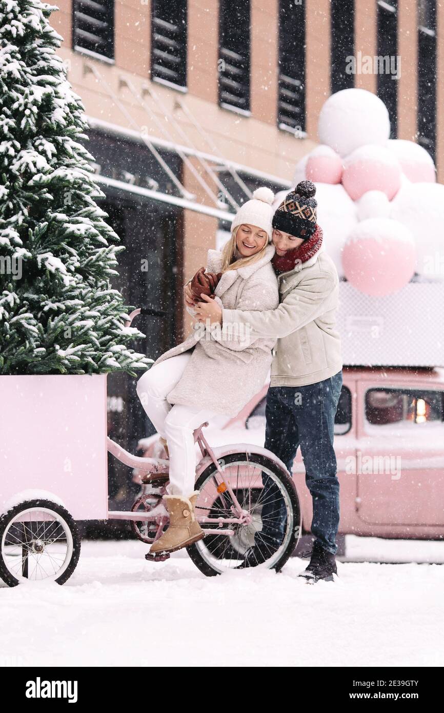 Paar umarmt, Spaß im Winter vor Weihnachten, sitzen auf alten rosa Fahrrad während Schneefall Stockfoto