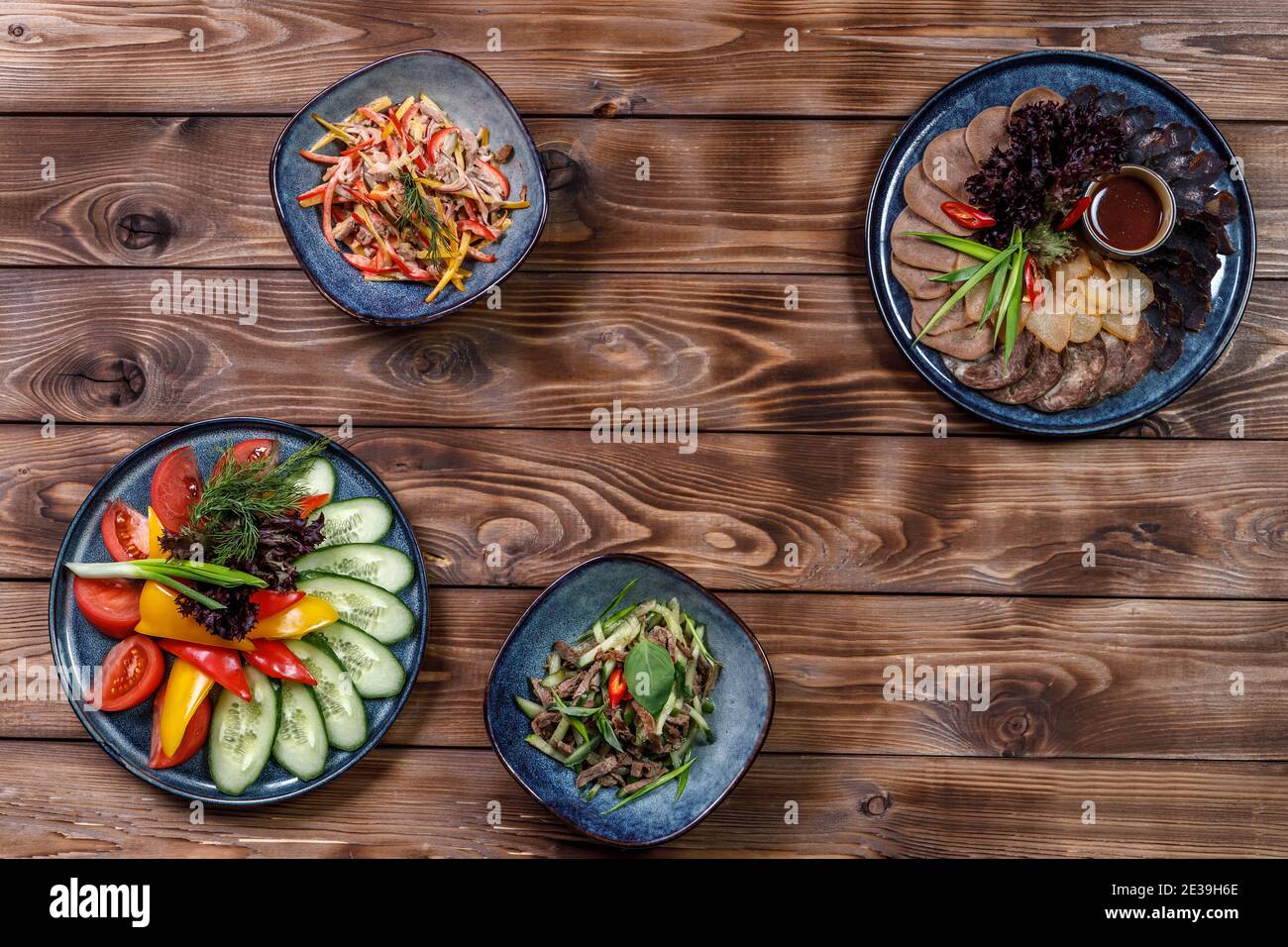 Flaches Layout verschiedener Gerichte mit geschnittenem Gemüse, Fleischstücken, Salaten auf braunem Holzhintergrund. Speicherplatz kopieren. Stockfoto