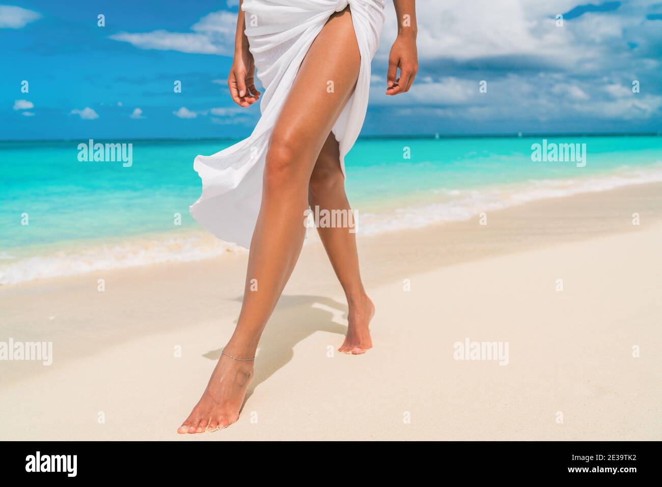 Elegante Frau, die am karibischen Strand mit schlanken, glatten Beinen läuft Für die Hautpflege Sonnenbräune tragen Cover-up Sarong Wrap Beachwear Rock entspannend auf tropischen Stockfoto