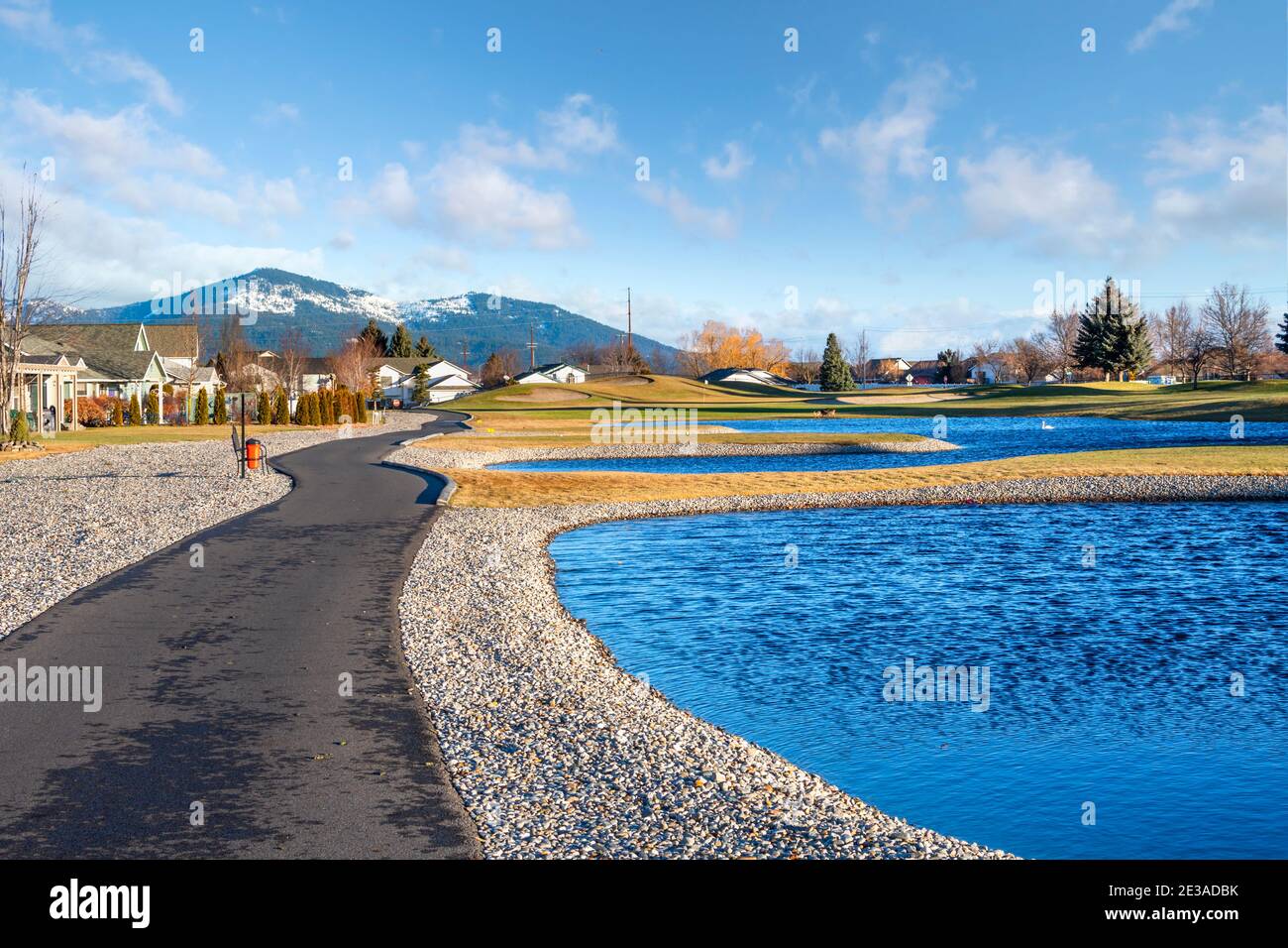 Ein Wanderweg und Wassergefahr umgeben von Häusern in der Prairie Falls Golf Course Gemeinschaft in Post Falls, Idaho, mit Rathdrum Mountain in Sicht. Stockfoto