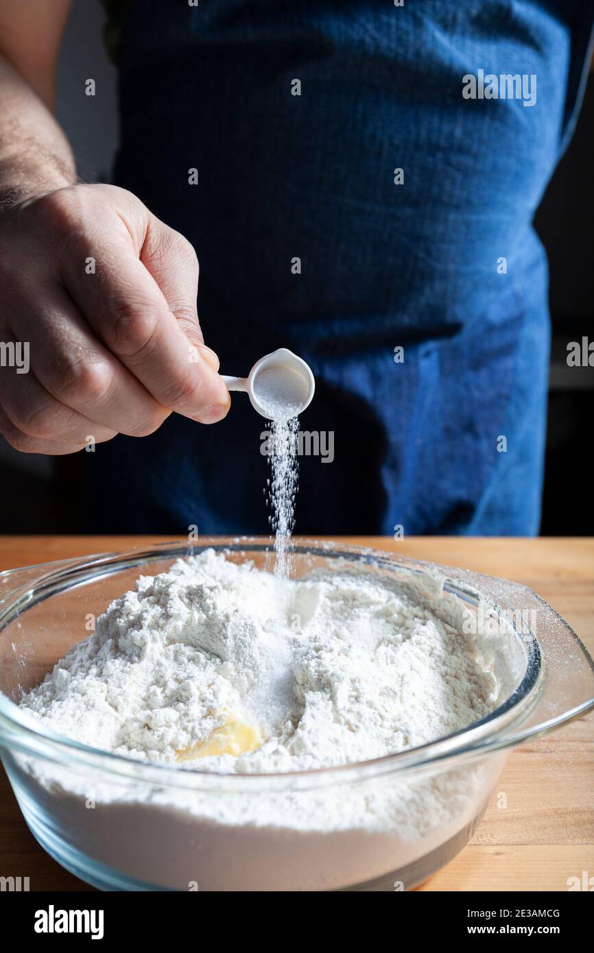 Die männlichen Hände des Bäckers geben dem Mehl Salz hinzu. Teigzubereitung Stockfoto