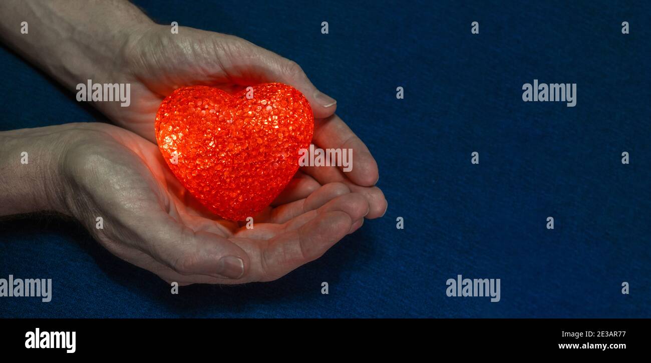 Rot flammendes Herz in kräftigen männlichen Händen auf blauem Hintergrund. Valentinstag-Konzept. Das Thema der Liebe und Sorge für die Gesundheit Ihres Herzens. Banner. Stockfoto Rot flammendes Herz in kräftigen männlichen Händen auf blauem Hintergrund. Valentinstag-Konzept. Das Thema der Liebe und Sorge für die Gesundheit Ihres Herzens. Banner. Stockfoto