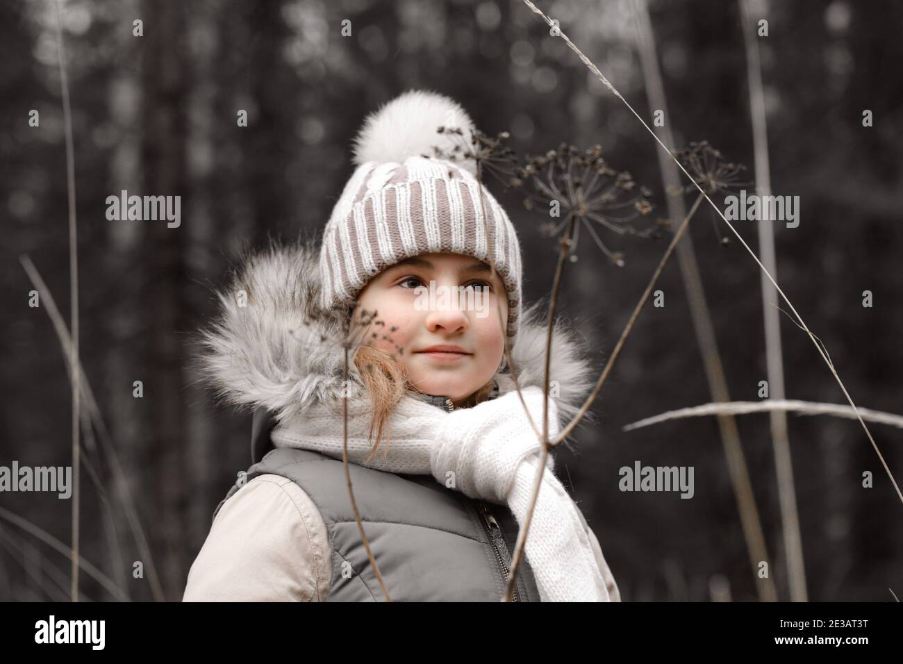Nettes Teenager-Mädchen in einem warmen Hut und Schal auf dem Hintergrund eines Herbstwaldes. Wintermode-Bekleidung Stockfoto