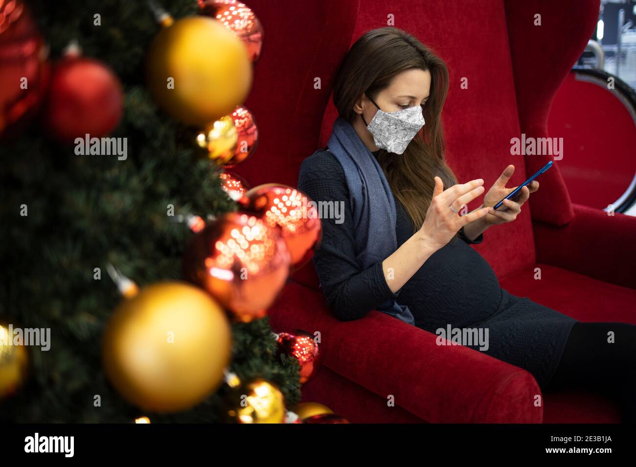 Schwangere Frau mit einer Gesichtsmaske SMS drinnen Stockfoto
