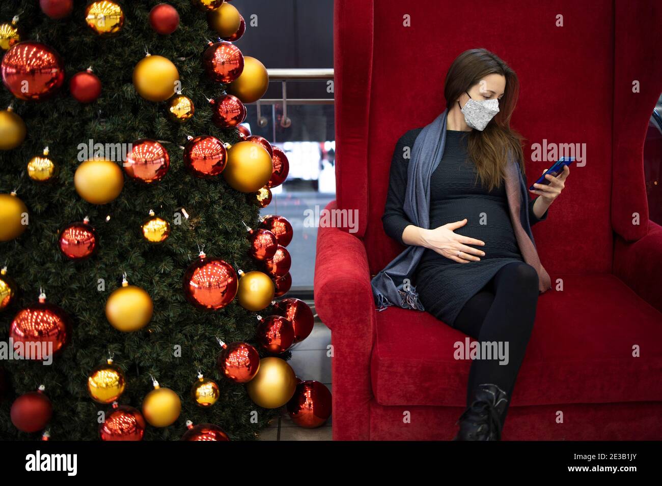 Schwangere Frau mit einer Gesichtsmaske SMS drinnen Stockfoto