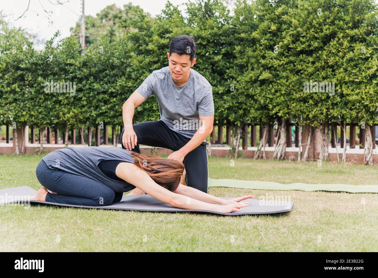 Asiatische Mann und Frau Training Yoga im Freien in meditieren Pose sitzen auf grünem Gras. Junges Paar üben Stretching tun in der Natur einen Feldgarten Stockfoto