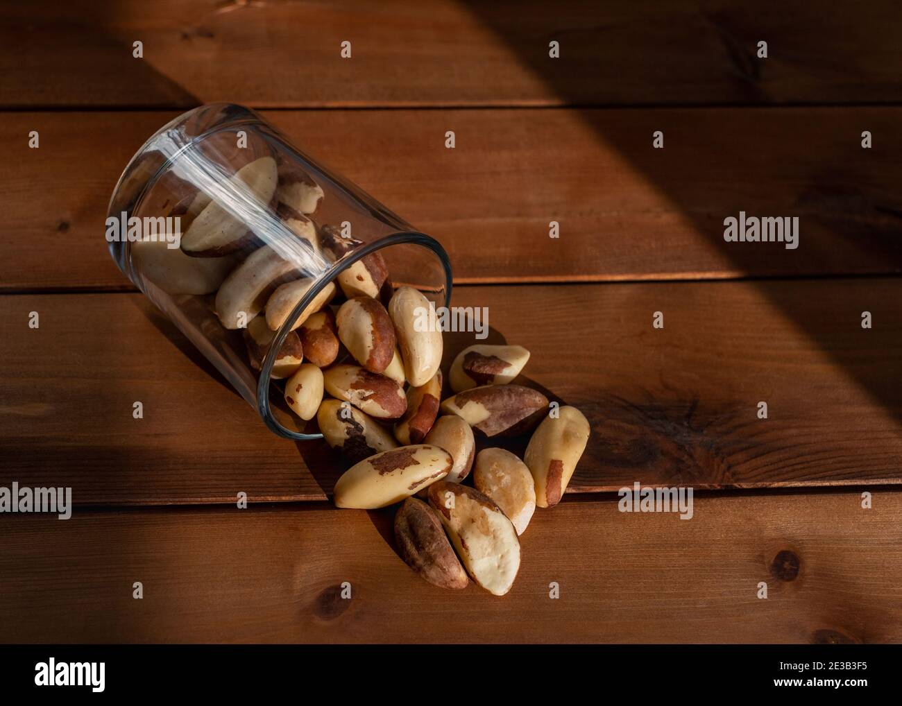 Verstreute Paranüsse unter natürlichem Sonnenlicht auf Holztisch. Gesunde Lebensmittel und Snacks Stockfoto