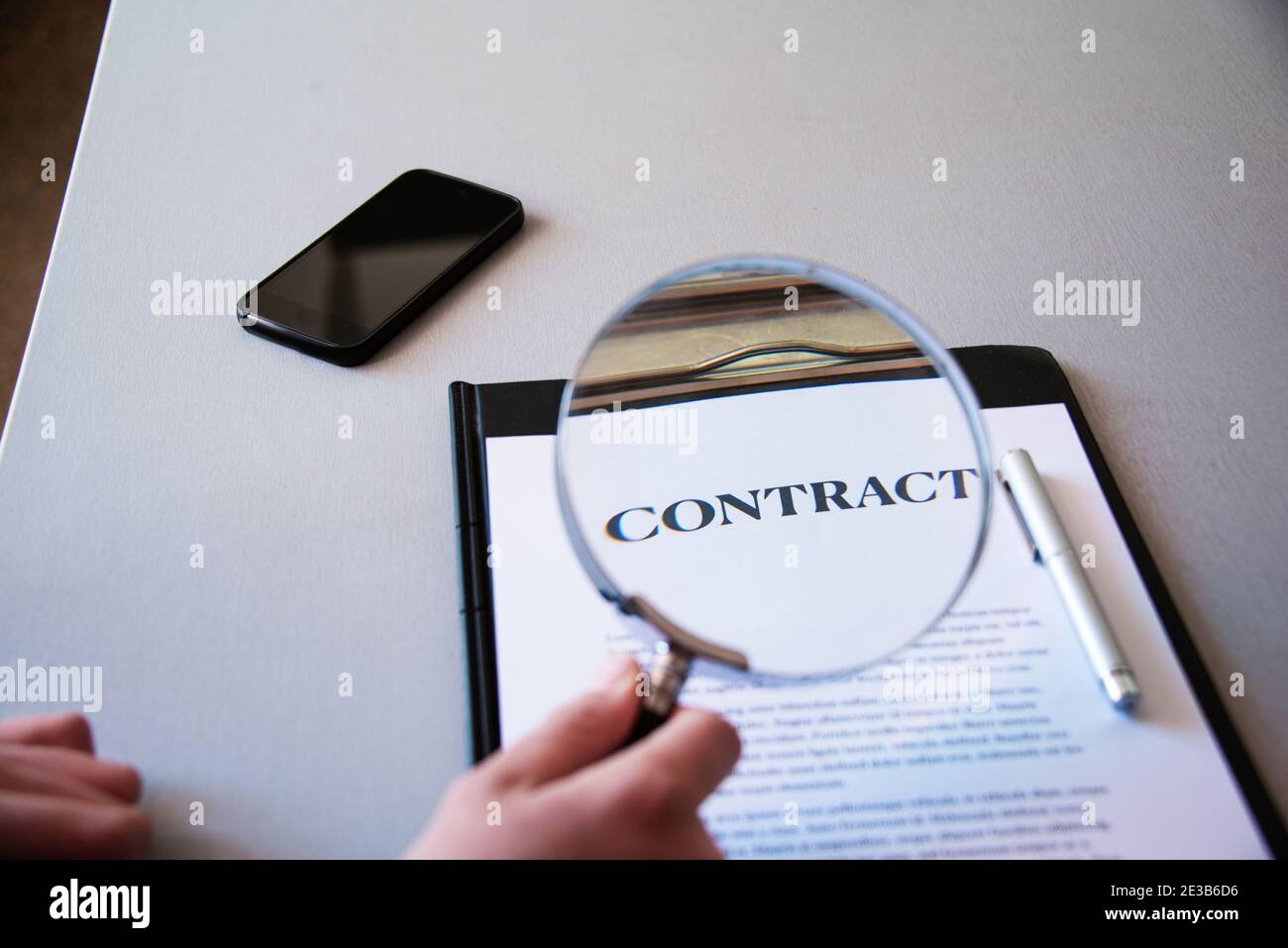 Junger Mann, der den Kontakt mit einer Lupe betrachtet, den kleinen Druck überprüft, Haus kauft oder von zu Hause aus arbeitet; selektiver Fokus Stockfoto