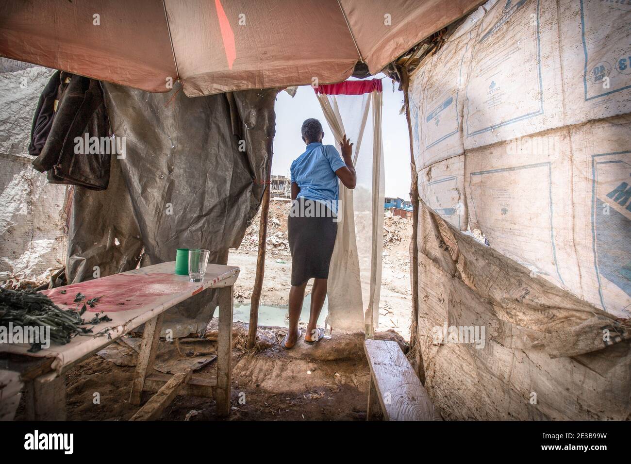 Eine Frau steht neben ihrem kleinen Restaurant aus gebrauchten Polypropylen-Säcken. In Afrikas größten und langsam entwickelnden Kibera-Slums, bekannt für ihr höchstes Bevölkerungswachstum und die dichte Verbindung und Nähe von Strukturen rund um die Nachbarschaften, Nicht jeder ist in der Lage, Recycling von Abfallprodukten und Kunststoffprodukten zu üben und zu handeln. Nach dem Abriss von Häusern und Geschäften, die sich in der Nähe der Eisenbahnlinie der Kenya Railways befinden, werden die meisten Bewohner gesehen, wie sie das Recycling von Polypropylensäcken praktizieren, um ihre neuen Häuser und kleinen Geschäfte zu bauen, sowie wir Stockfoto