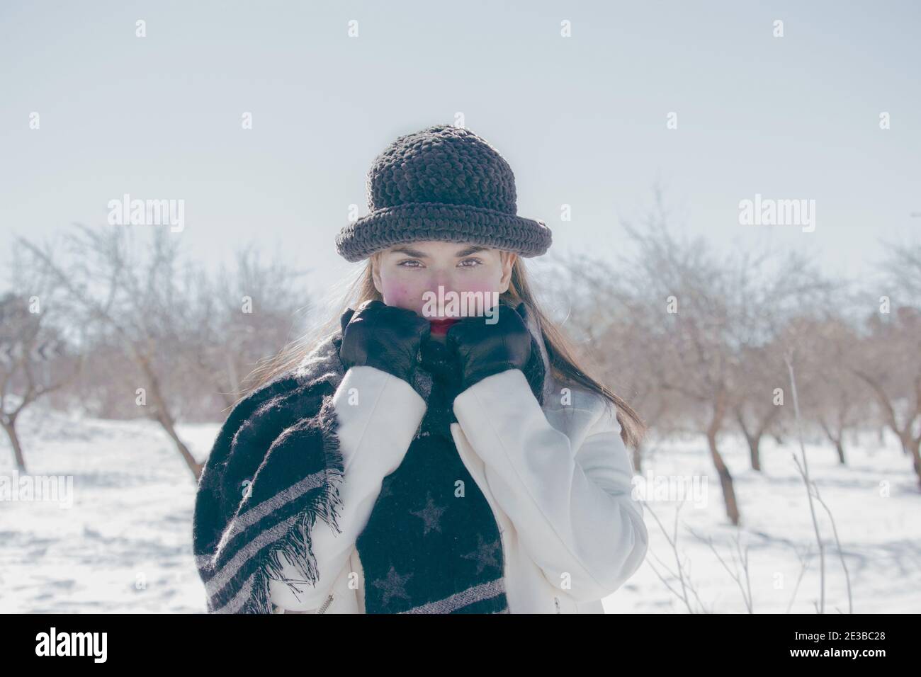Porträt einer attraktiven jungen Frau lächelt in warmer Kleidung an einem kalten Tag in einem Hintergrund in der Natur verschneit. Winter im Freien 2021. Stockfoto